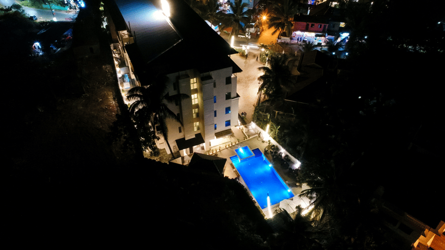 Aerial view of Amara Grand Baga, Goa, at night with a swimming pool in front.